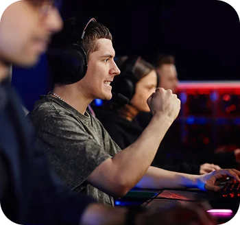 Drużyna e-sportowa grająca na komputerach do gier, jeden z graczy świętuje ważny moment, nosząc słuchawki podczas intensywnego meczu online.