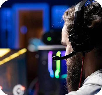 Widok z boku profesjonalnego gracza e-sportowego z gamingowymi słuchawkami, skupionego na rywalizacyjnym meczu w ustawieniu do gier z oświetleniem RGB.