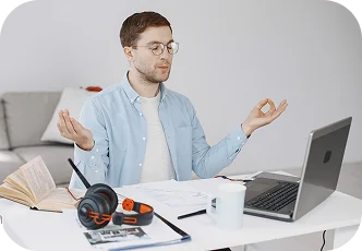 Młody mężczyzna medytuje przy biurku, ucząc się na laptopie, skupiając się i kontrolując stres podczas nauki online.